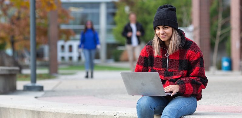 Student outside in fall working on laptop